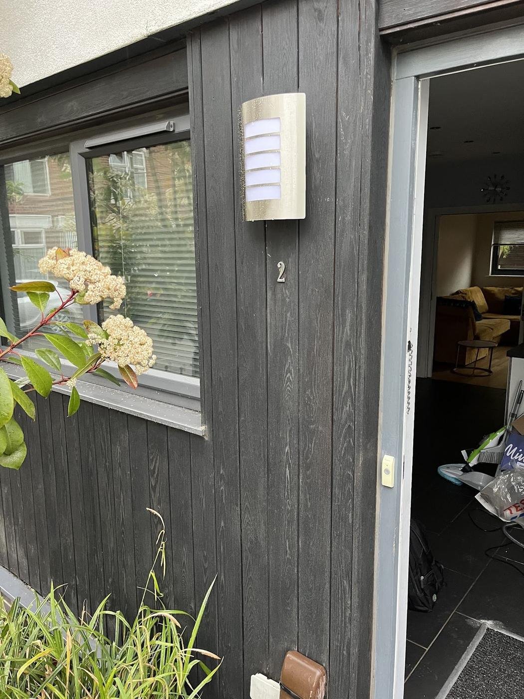 Outdoor wall light fitted beside a dark timber-clad door