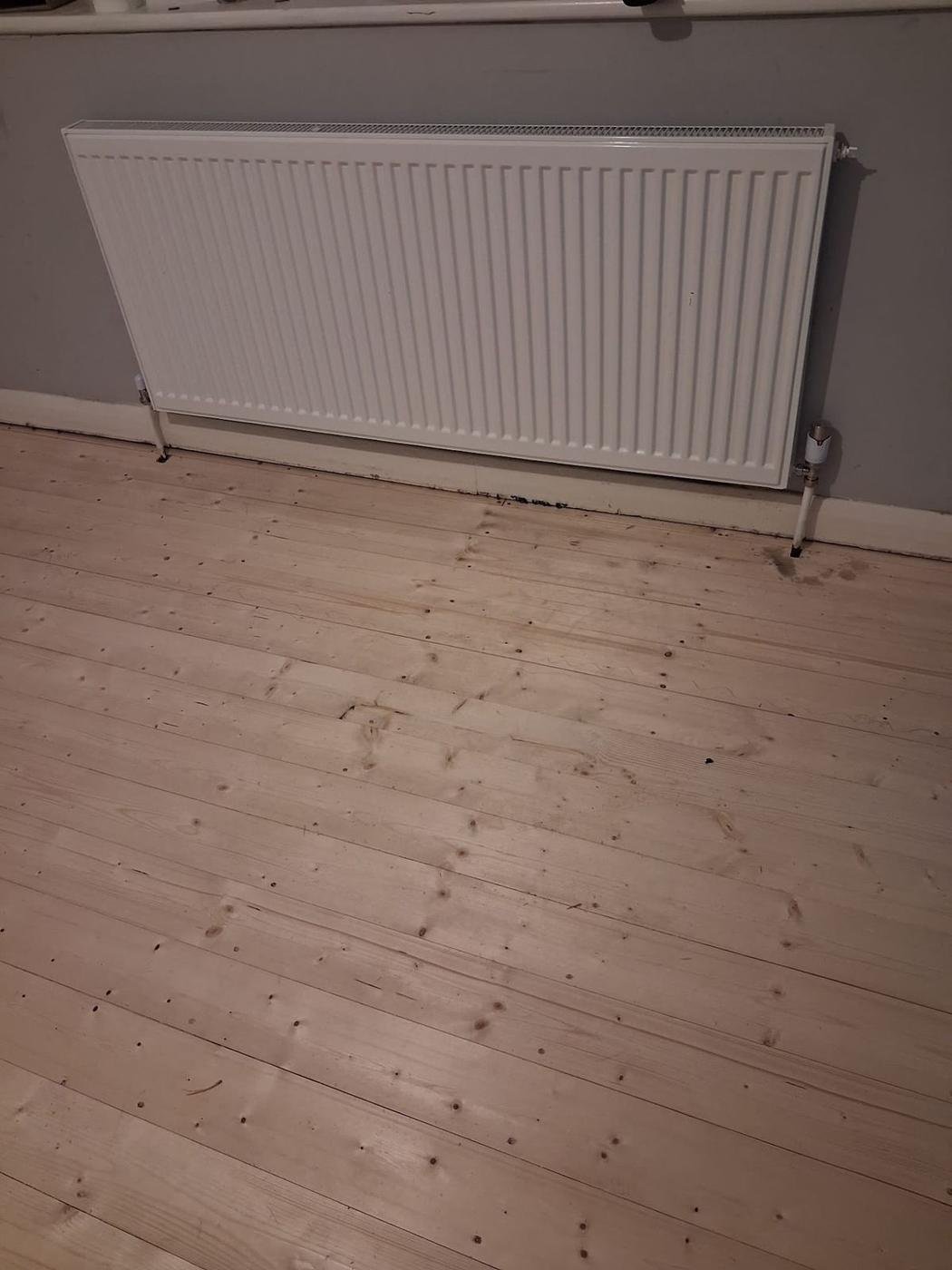 A white radiator above sanded floorboards