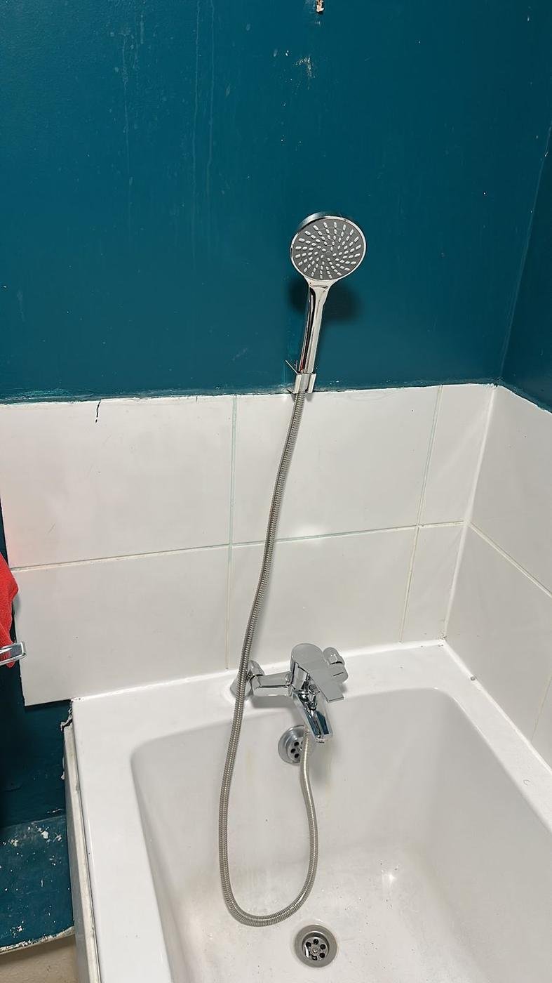 A bath shower mixer against a teal wall